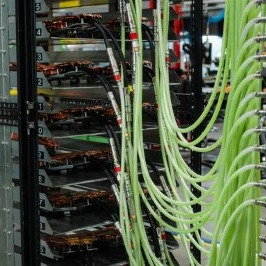 A tall industrial testing rack holding multiple horizontal hardware units, with dozens of translucent green hoses and black cables connected to the front of the assembly.
