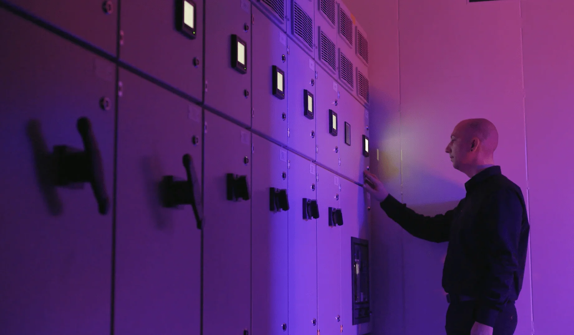 Data center engineer monitoring control panels in a server room, illuminated by purple lighting while adjusting system settings.