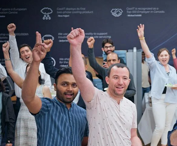 A large group of diverse employees at CoolIT Systems cheering and raising their fists in celebration during an indoor company gathering.