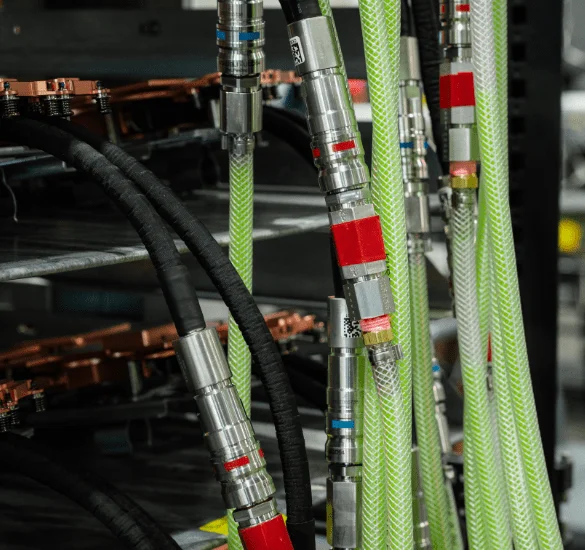 A close-up of a series of vertical, translucent green hoses with silver metal connectors and red and blue markings, organized in a dense row.