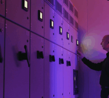 Data center engineer monitoring control panels in a server room, illuminated by purple lighting while adjusting system settings.