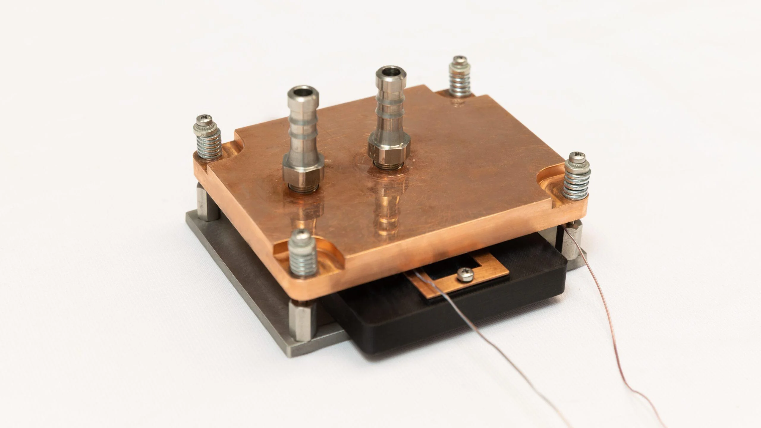A high-angle shot of a square copper cooling plate with two vertical metal nozzles and mounting screws, shown as a standalone hardware component on a white surface.
