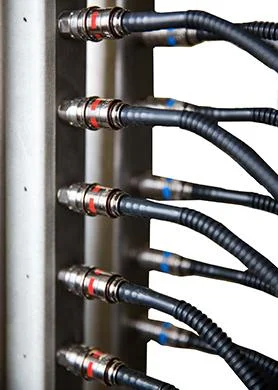 A close-up side view of a vertical silver metal manifold with multiple black hoses securely attached using metal connectors marked with red and blue bands.