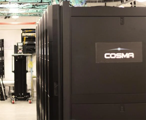 A row of black industrial server cabinets in a data center facility, with a "COSMA" logo badge visible on the front of the primary rack.