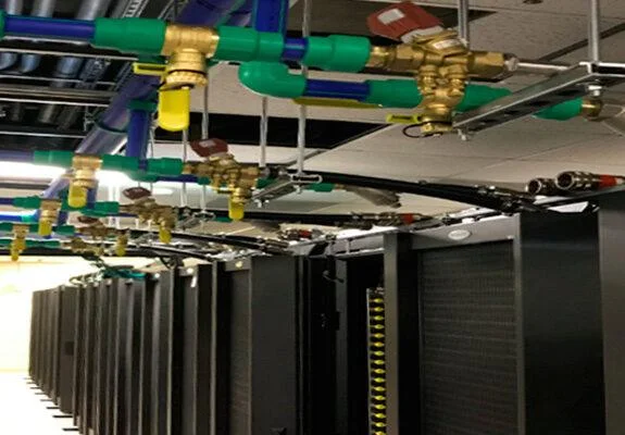 High-density HPC data centre racks with overhead liquid cooling piping supplying coolant to servers.