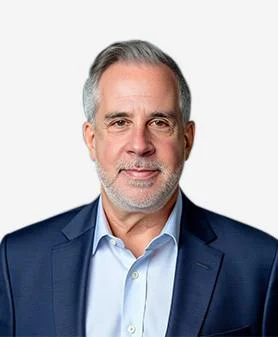 A professional headshot of Jason Waxman, smiling and wearing a blue suit jacket over a light blue dress shirt.