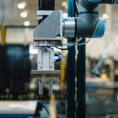 A detailed shot of a high-precision robotic mechanical tool with metal prongs and blue air hoses, used for automated hardware assembly in a factory setting.