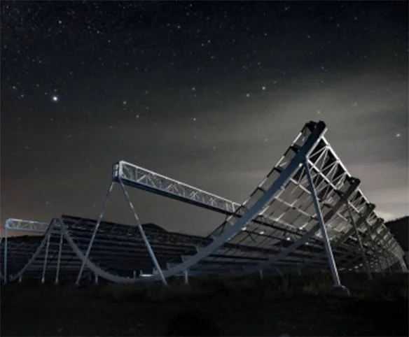A wide nighttime shot of the CHIME radio telescope's large metal cylindrical reflectors under a vast, star-filled sky.