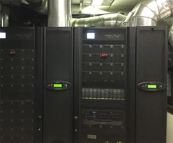 A row of black industrial server racks installed in a utility room with large silver ventilation ducts running overhead.