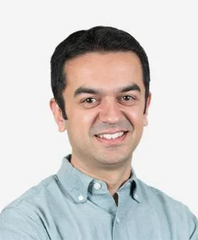 A professional headshot of Neil Mulji, smiling and wearing a light blue button-down shirt.