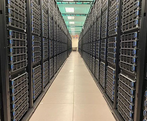 A perspective view looking down a long, symmetrical aisle between two rows of tall, black server racks in a brightly lit data center.